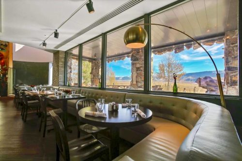 Cozy restaurant interior with a curved booth, tables set for dining, and large windows showcasing a scenic view.