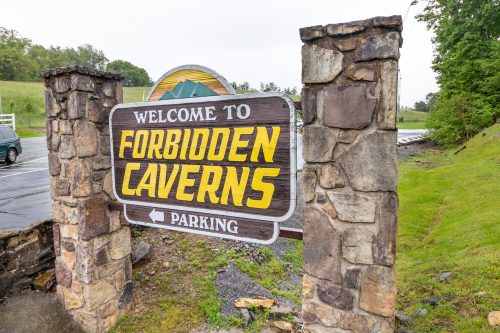 Sign at the entrance of Forbidden Caverns, featuring bold yellow lettering and stone pillars, with a parking direction.