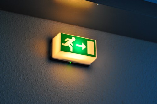 Green exit sign with a running figure and an arrow pointing to the right, illuminated on a wall.