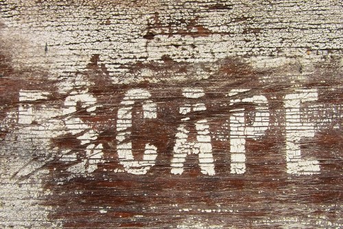 Faded white letters spelling "ESCAPE" on a weathered wooden surface.