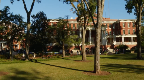 A historic building surrounded by trees and a grassy area, with people walking and enjoying the outdoors.