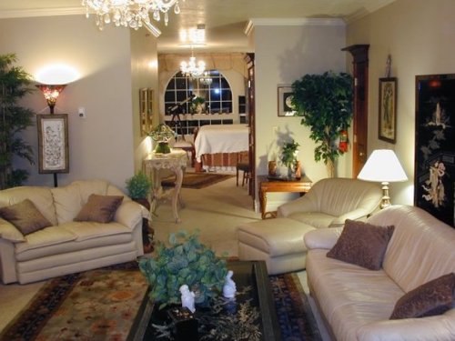 Cozy living room with beige sofas, a decorative rug, plants, and elegant lighting, leading to a dining area.