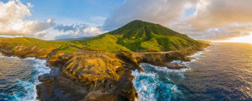 A scenic view of a green mountain by the ocean, with rocky shores and a vibrant sky at sunset.