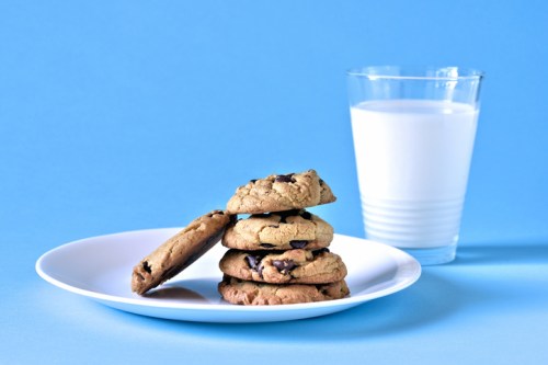 A plate of chocolate chip cookies stacked beside a glass of milk on a blue background.