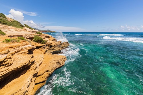 A rocky coastline with turquoise waters and gentle waves under a clear blue sky.