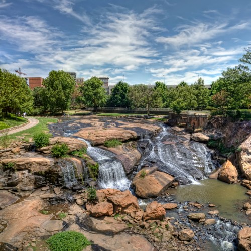 A scenic view of a waterfall cascading over rocks, surrounded by greenery and a clear blue sky.