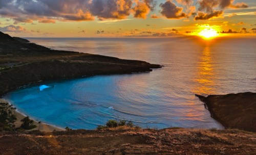 A stunning sunset over a tranquil bay, with vibrant colors reflecting on the water and clouds in the sky.