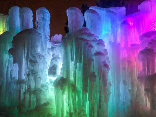 Colorful ice formations illuminated in shades of blue, green, and purple against a dark background.