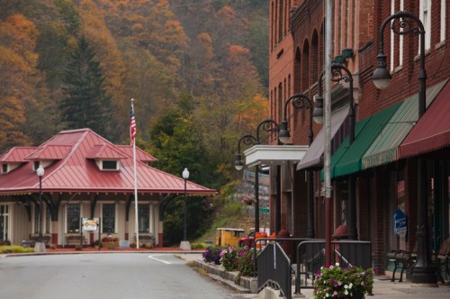 A quaint street scene featuring brick buildings, a train station, and autumn foliage in the background.