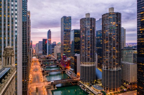 Aerial view of Chicago's skyline at dusk, featuring tall buildings and the Chicago River illuminated by city lights.