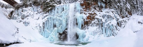 A frozen waterfall surrounded by icy cliffs and snow-covered ground, creating a serene winter landscape.