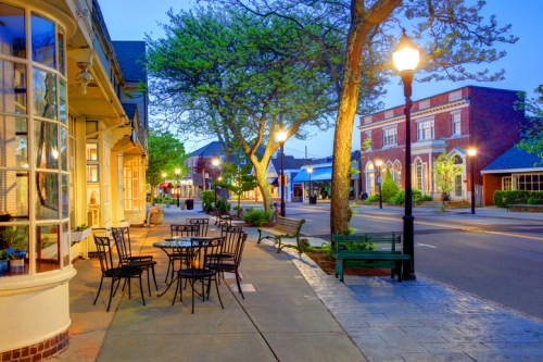 Charming street scene at dusk with outdoor seating, trees, and historic buildings illuminated by street lamps.