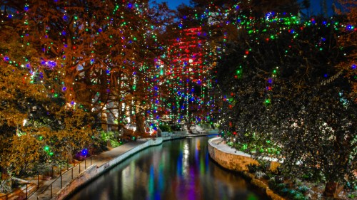 A serene river scene illuminated by colorful holiday lights on trees, creating a festive atmosphere at night.