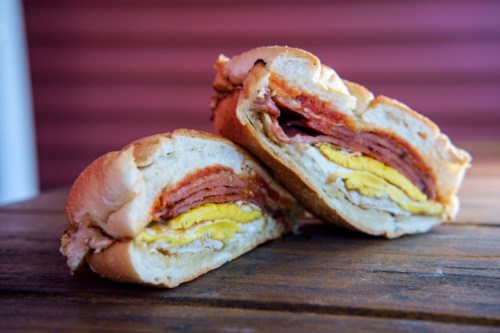 A close-up of a sliced sandwich with layers of meat and egg on a wooden surface.