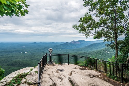 A scenic overlook with a viewing platform, surrounded by lush green mountains under a cloudy sky.
