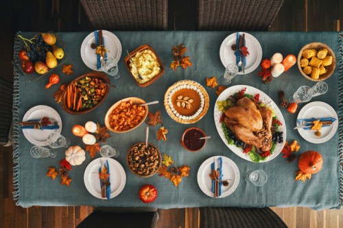 A beautifully set dining table with a turkey, sides, desserts, and autumn decorations for a festive meal.