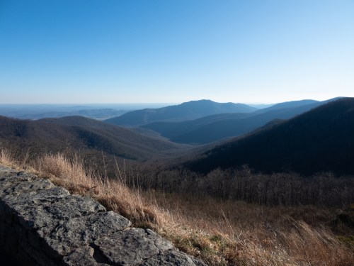 A panoramic view of rolling mountains under a clear blue sky, with grassy slopes in the foreground.