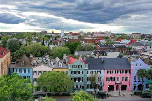 Aerial view of colorful historic buildings in a city, with greenery and a cloudy sky in the background.