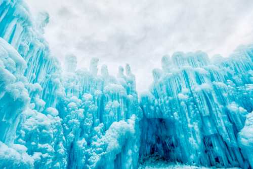 A stunning ice cave with towering blue ice formations under a cloudy sky.