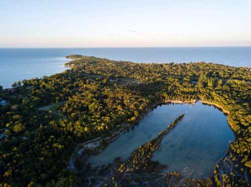 Aerial view of a lush green landscape meeting a calm blue lake and ocean under a clear sky.