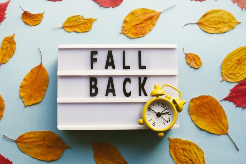 Lightbox with "FALL BACK" text and a yellow alarm clock, surrounded by autumn leaves on a blue background.