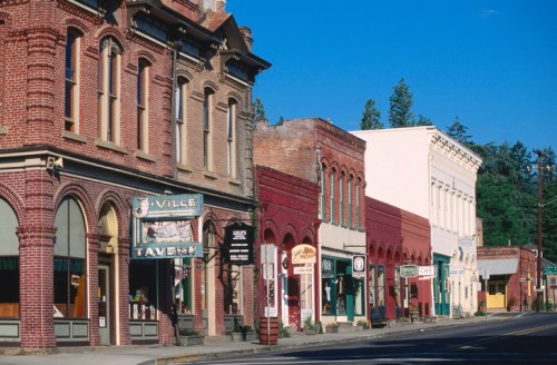 Historic brick buildings line a quiet street, showcasing various shops and a tavern under a clear blue sky.