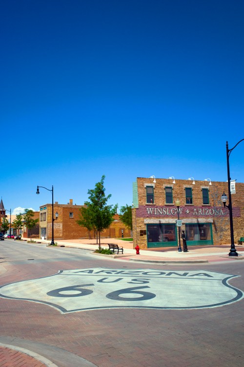 A sunny street view in Winslow, Arizona, featuring a Route 66 sign and historic buildings.