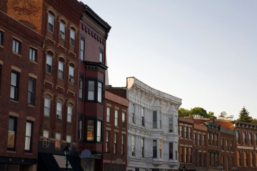 Historic buildings line a street, showcasing a mix of architectural styles and colors under a clear sky.