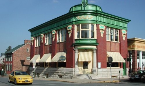 Historic brick building with green accents and large windows, featuring striped awnings and a yellow taxi parked outside.