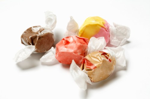 Four colorful wrapped candies in various flavors, including brown, pink, yellow, and red, on a white background.
