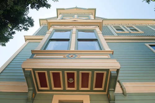 A low-angle view of a colorful Victorian-style house with intricate window details and decorative trim.