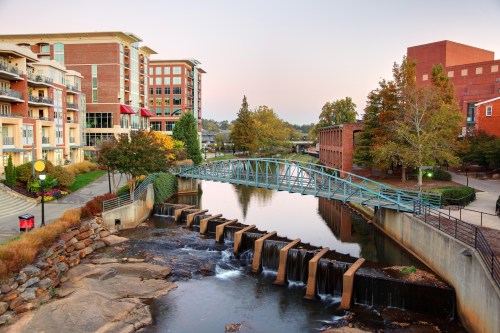 A scenic view of a river with a blue bridge, surrounded by buildings and trees, during sunset.