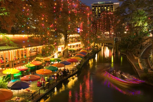 A vibrant riverside scene with colorful umbrellas, festive lights, and a boat gliding through the water at night.