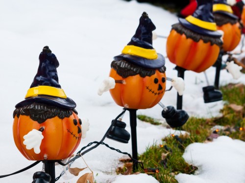 Colorful pumpkin decorations with hats line a snowy yard, adding a festive touch to the winter landscape.