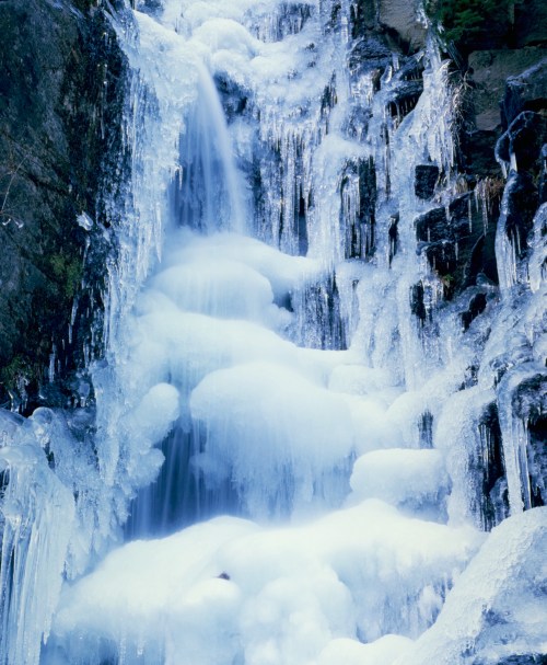 A frozen waterfall cascading down rocky cliffs, surrounded by ice formations and snow.