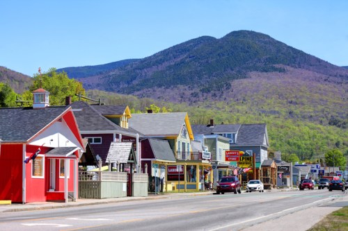 A charming street lined with colorful buildings, set against a backdrop of green mountains under a clear blue sky.