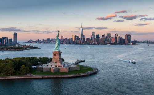 Aerial view of the Statue of Liberty with the New York City skyline in the background during sunset.