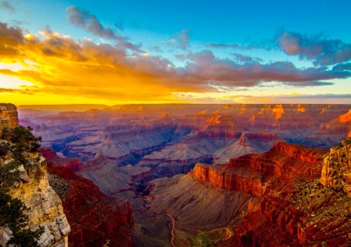 A stunning sunset over the Grand Canyon, highlighting vibrant orange and red rock formations under a colorful sky.