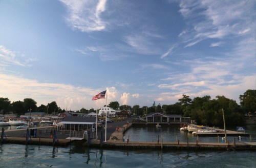 A marina with boats docked, an American flag waving, and a blue sky with scattered clouds in the background.