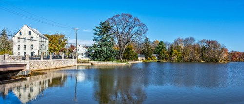 A serene lake scene with trees and a white building reflecting on the water under a clear blue sky.