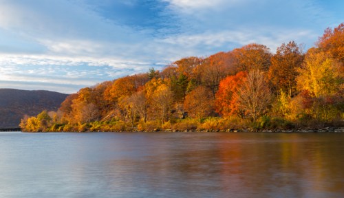 A serene river scene with vibrant autumn foliage reflecting on the water under a clear blue sky.