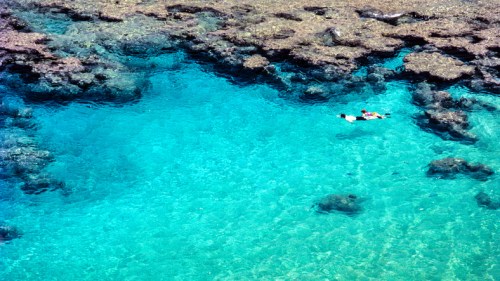 Aerial view of two people swimming in clear turquoise water over a coral reef.
