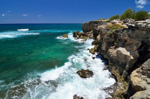 A rocky coastline with turquoise waves crashing against the shore under a clear blue sky.