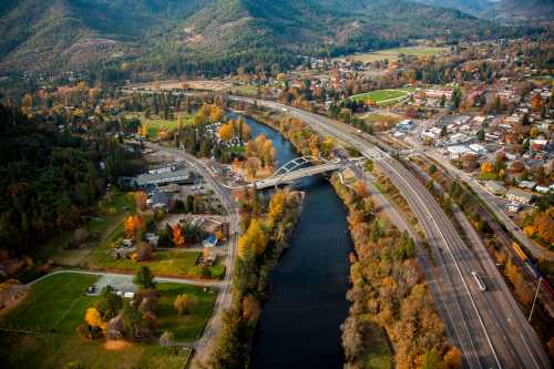 Aerial view of a river winding through a valley, surrounded by autumn foliage and a small town with roads and bridges.