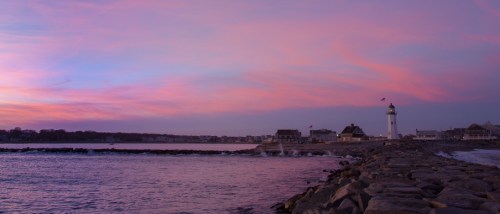 A serene sunset over a coastal scene featuring a lighthouse and rocky shoreline, with colorful skies reflecting on the water.