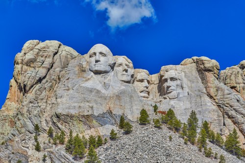 Mount Rushmore featuring the carved faces of four U.S. presidents against a blue sky and rocky landscape.