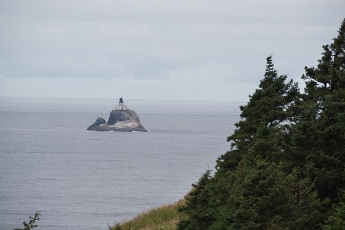 A lighthouse on a rocky island in the ocean, surrounded by calm waters and a green shoreline in the foreground.