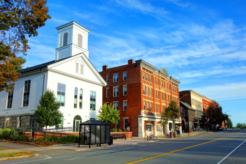A street view featuring a white church and historic brick buildings under a blue sky with scattered clouds.