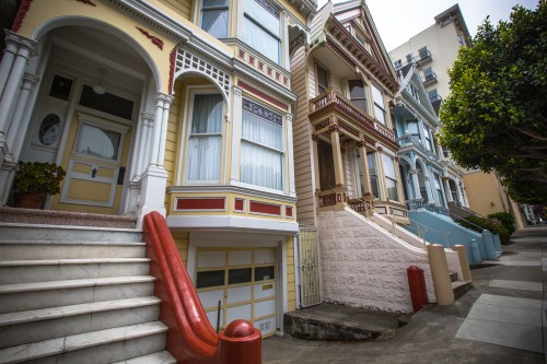 Colorful Victorian houses line a sidewalk, showcasing intricate architectural details and vibrant paint colors.