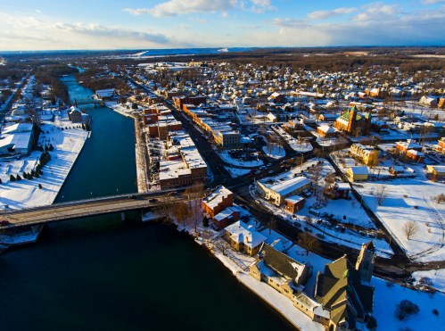 Aerial view of a snowy town with a river, bridges, and colorful buildings under a clear blue sky.